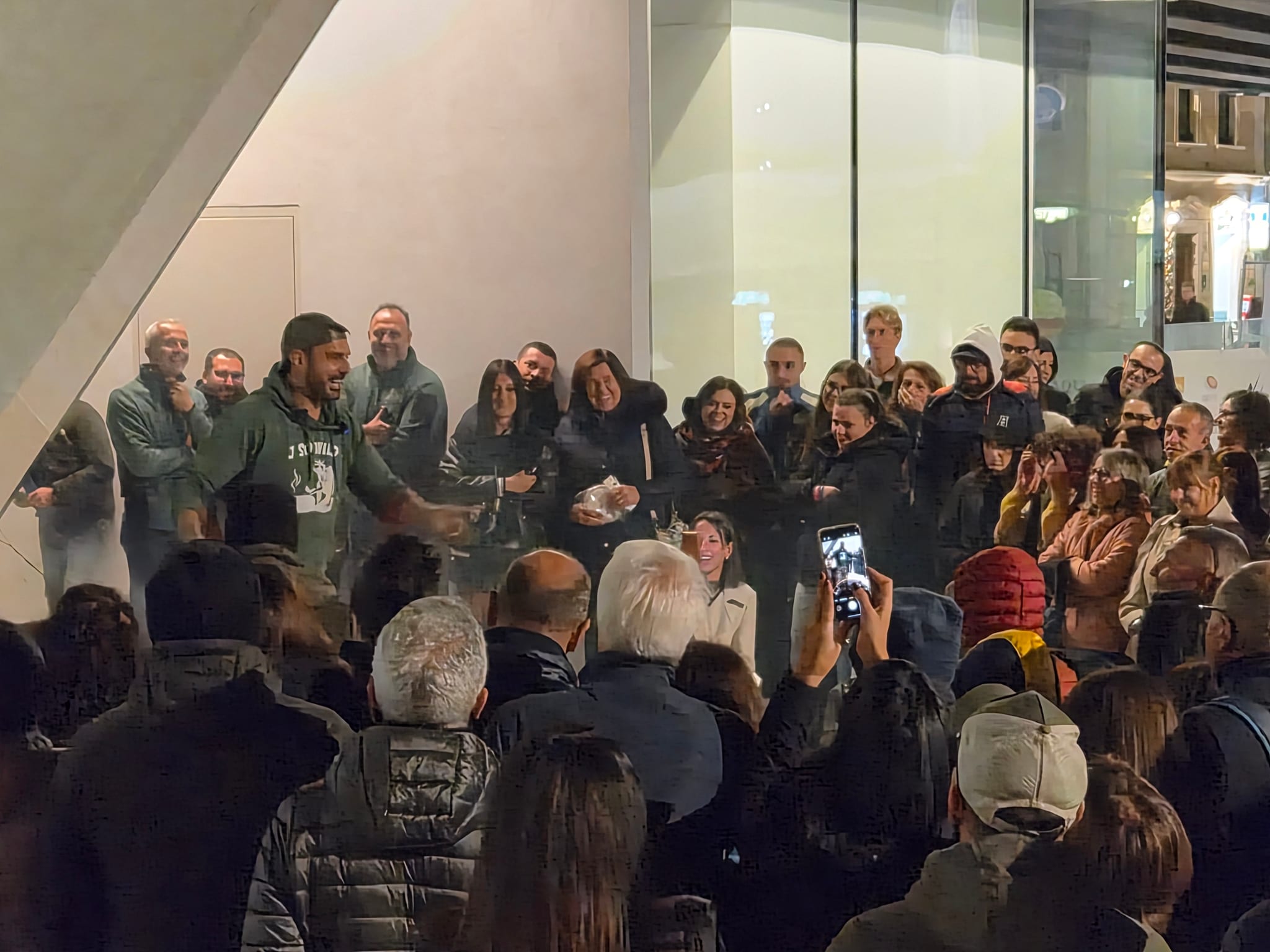 Uno chef con cappellino e grembiule cucina davanti al pubblico che lo osserva e fotografa